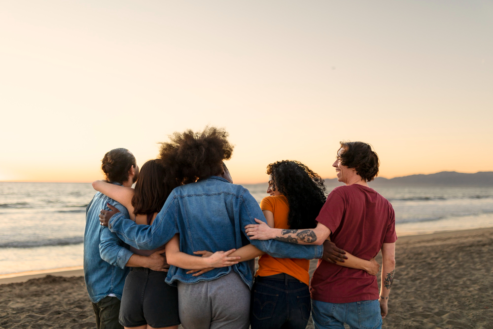 a group of five adults walk on the beach with their arms around each other